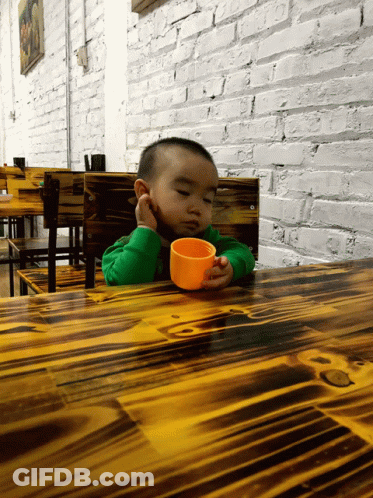 Little Boy Sitting At Table With Cup GIF