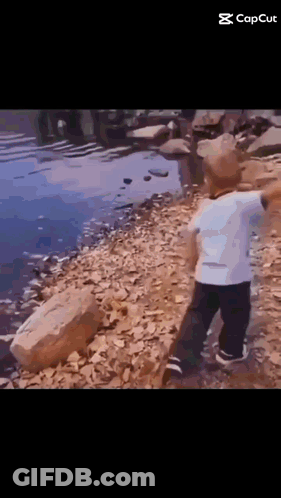 Little Boy Standing On Rock Near Water GIF