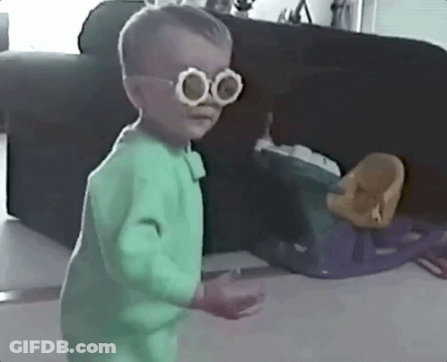 Little Boy With Glasses And Green Outfit Beside Couch GIF
