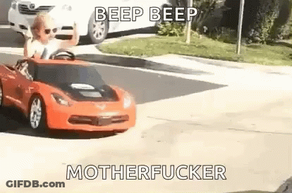 Little Girl Driving Red Toy Car Down Street GIF
