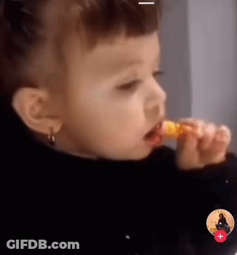 Little Girl Eating Yellow Lollipop With Red Plus Sign GIF