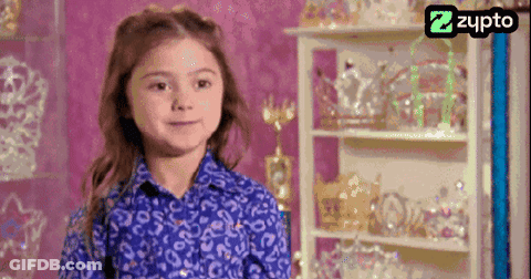 Little Girl In Blue Shirt Smiling In Front Of Crown Shelf GIF