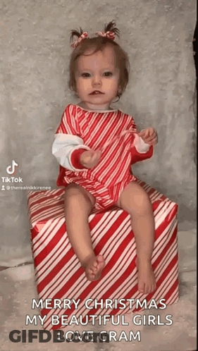 Little Girl In Candy Cane Outfit Sitting On Candy Cane Box GIF