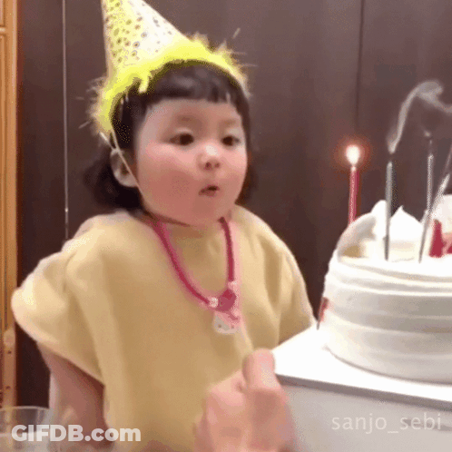 Little Girl In Party Hat Standing In Front Of Birthday Cake GIF