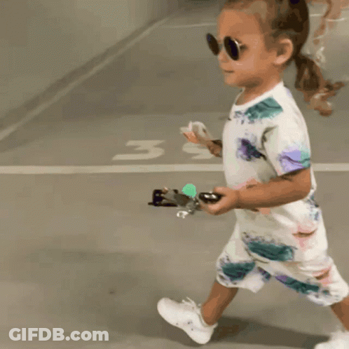 Little Girl In Sunglasses And Floral Outfit Walking In Parking Lot GIF