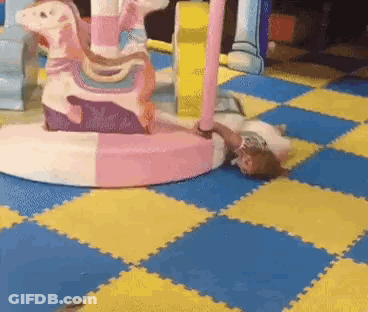 Little Girl Laying On Floor In Front Of Carousel GIF
