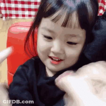 Little Girl Smiling On Red Couch Held By Person GIF