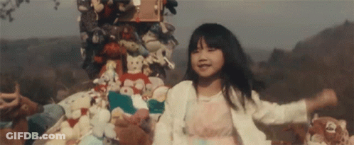 Little Girl Standing In Front Of Stuffed Animals And Toys GIF
