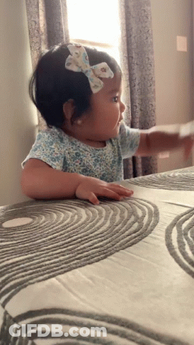 Little Girl With Bow Sitting On Bed GIF
