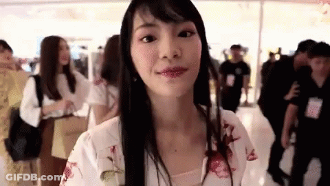 Long Black-Haired Woman Looking At Camera In Mall GIF