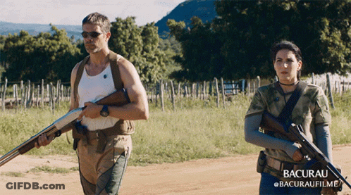 Man And Woman Holding Guns In Field Bacurau GIF
