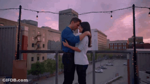 Man And Woman Hugging On Balcony Overlooking City Sunset GIF