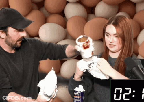 Man And Woman In Front Of Egg Wall And Clock GIF