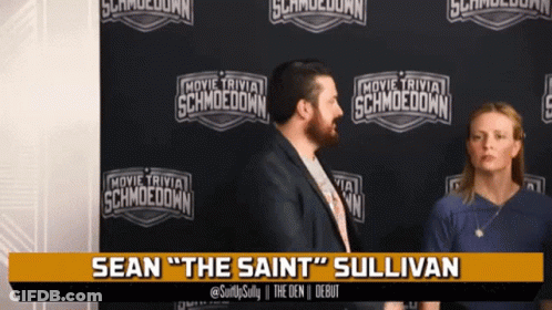 Man And Woman In Front Of Movie Trivia Schmoodown Wall GIF