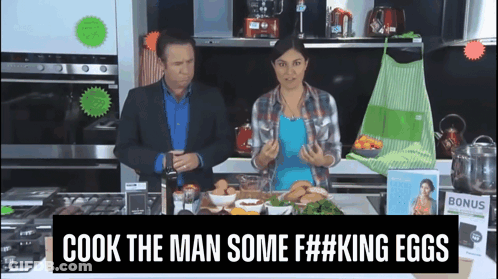 Man And Woman In Kitchen With Sign Saying Cook The Man Some F##king Eggs GIF