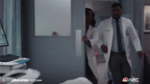 Man And Woman In Lab Coats Walking In Hospital Hallway With NBC GIF
