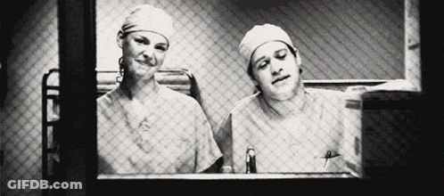 Man And Woman In Scrubs Looking Out Window GIF