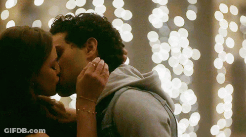 Man And Woman Kissing In Front Of Christmas Lights GIF