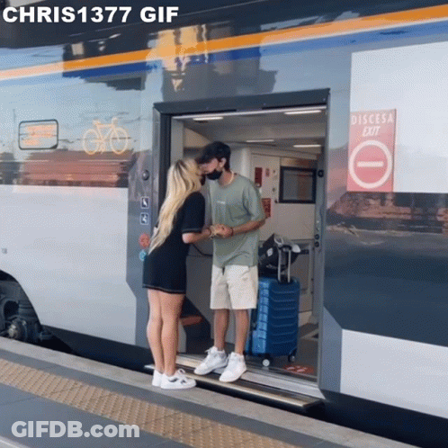 Man And Woman Kissing In Front Of Train With Discesa Exit Sign GIF