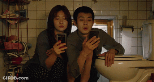 Man And Woman Looking At Phones In Bathroom GIF