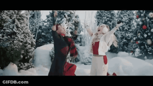 Man And Woman Playing In Snow With Christmas Trees GIF