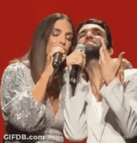 Man And Woman Singing Into Microphones On Stage GIF