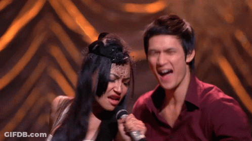 Man And Woman Singing Into Microphones On Stage GIF