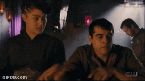 Man And Woman Sitting At Table With CW Logo GIF