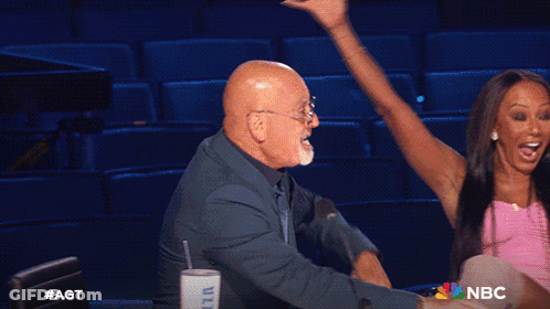 Man And Woman Sitting In Front Of AGT Sign GIF