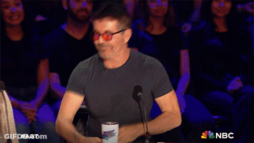 Man And Woman Sitting In Front Of AGT Sign GIF
