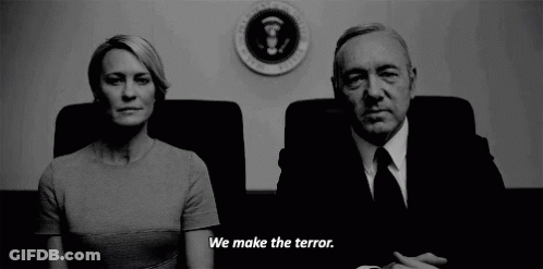 Man And Woman Sitting In Front Of Sign Saying We Make The Terror GIF
