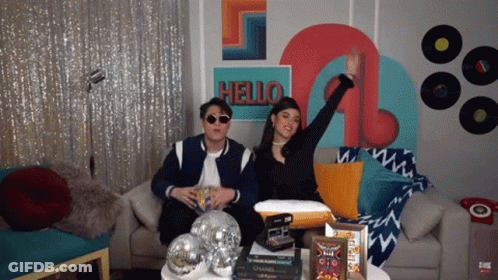 Man And Woman Sitting On Couch Before Hello Wall GIF
