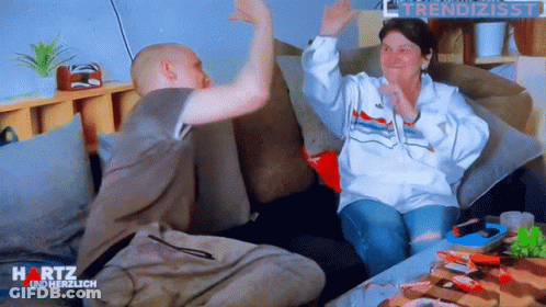 Man And Woman Sitting On Couch With Hartz On Bottom Right GIF