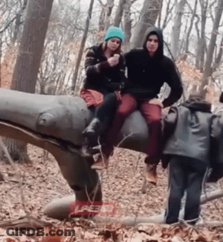 Man And Woman Sitting On Dinosaur Statue GIF