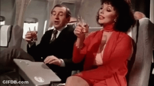 Man And Woman Sitting On Plane Holding Wine GIF