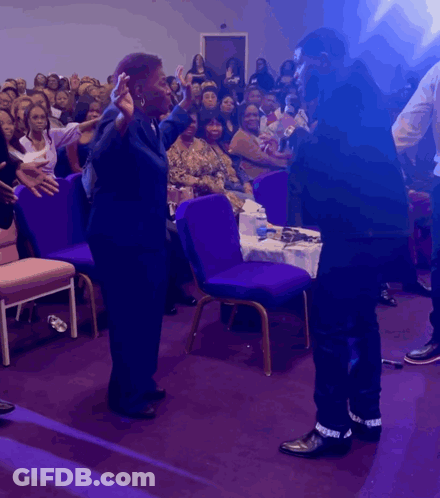 Man And Woman Stand Before Crowd In Purple Chairs GIF