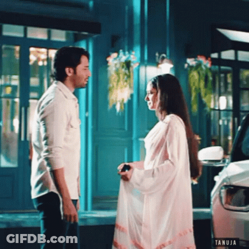 Man And Woman Standing In Front Of Building With Tanuja Logo GIF