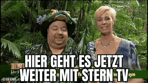 Man And Woman Standing In Front Of Hier Geht Es Jetzt Sign GIF