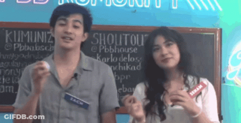 Man And Woman Standing In Front Of Shoutout Sign GIF
