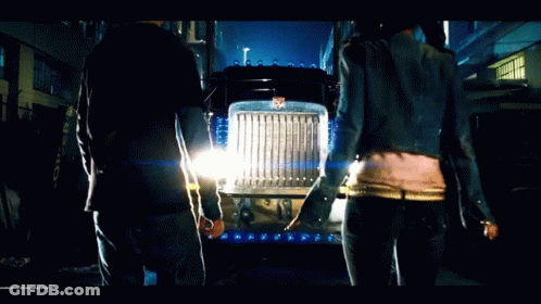 Man And Woman Standing In Front Of Transformers Semi Truck GIF