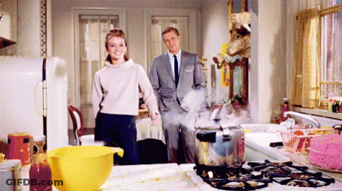 Man And Woman Standing In Kitchen Near Boiling Pot GIF