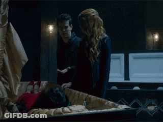 Man And Woman Standing Next To Coffin With Woman Inside GIF