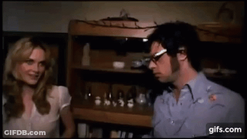 Man And Woman Talking By Bookshelf GIF