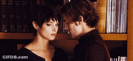Man And Woman Touching Foreheads In Front Of Bookshelf GIF