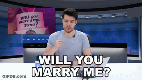 Man At Desk With Sign Saying Will You Marry Me Tana GIF