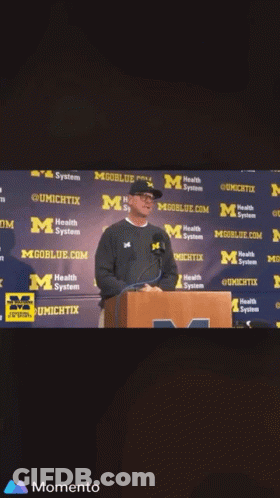 Man At Podium With Mgoblue.com Wall GIF
