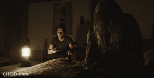 Man At Table In Dark Room With Lantern GIF