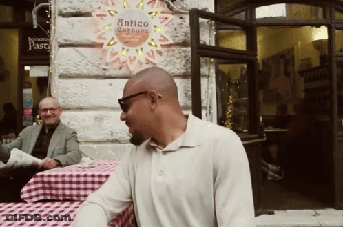Man At Table In Front Of Antico Carbone Sign GIF