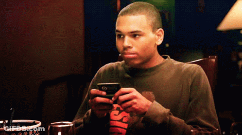Man At Table Looking At Phone In Chris Brown Shirt GIF