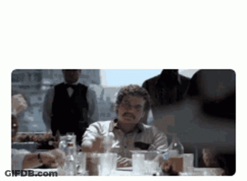 Man At Table With Glasses And Alcohol Bottles GIF